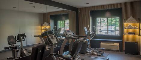 Une salle de sport équipée de machines de cardio, dotée d’un mur avec des miroirs et d’une fenêtre donnant sur les voitures garées.