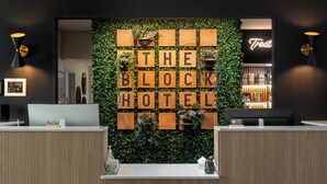 Una recepción con una pared de madera bloqueada que muestra “THE BLOCK HOTEL” y un letrero de neón que dice “Treat”.