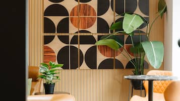 Um interior moderno com parede estampada em padrão geométrico, uma mesa redonda e uma área de estar com uma planta.