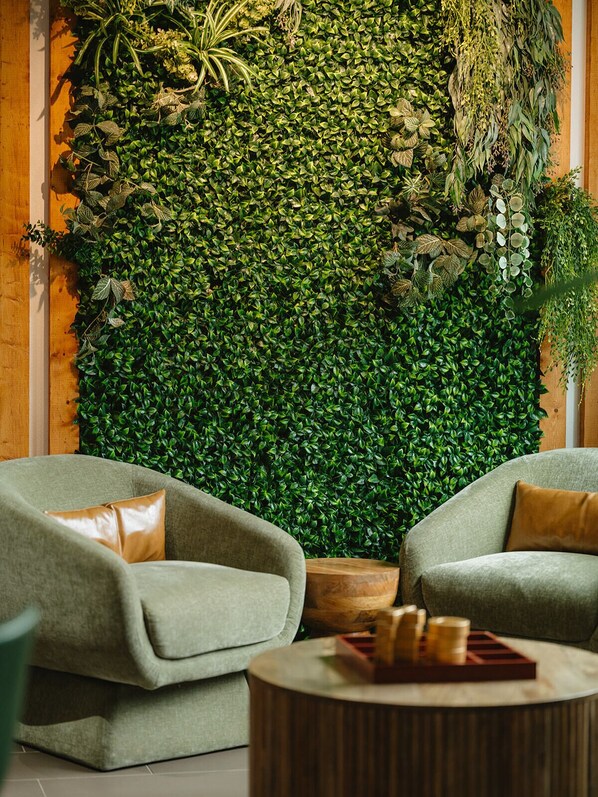 A room with two green armchairs, a round wooden coffee table, and a lush green vertical garden wall.