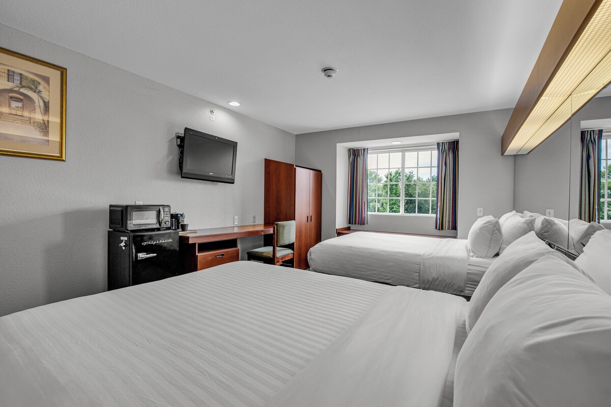 Une chambre d’hôtel avec deux lits, un bureau avec une télévision, un réfrigérateur et une fenêtre avec des rideaux.