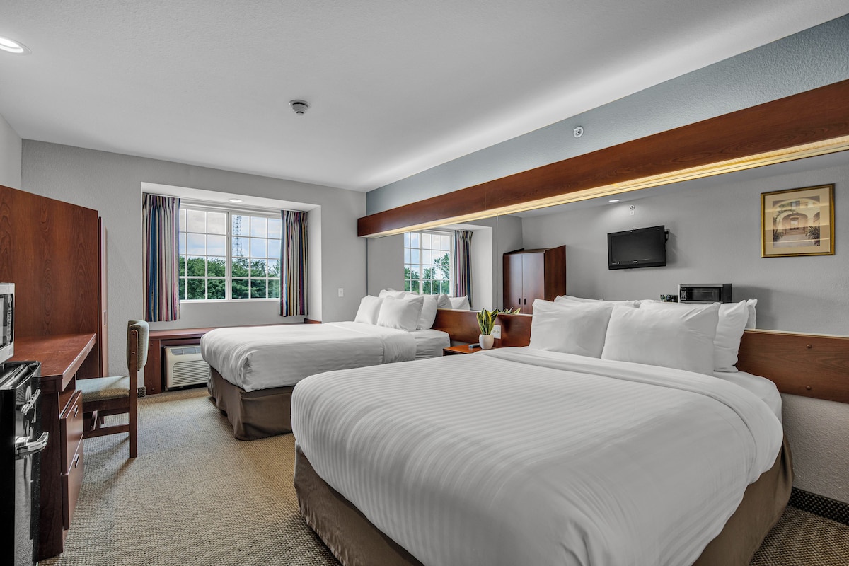 A hotel room with two beds, a desk, a TV, and a window with curtains.