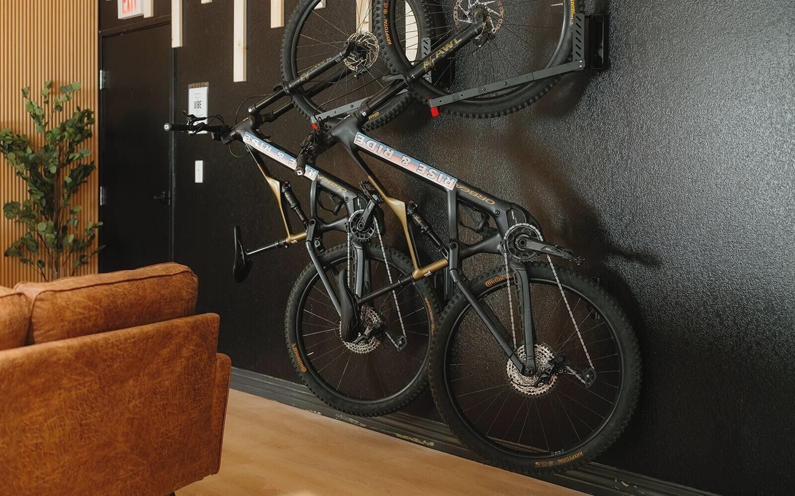 A room with a black wall, a brown sofa, and a bicycle mounted on a wall-mounted rack.
