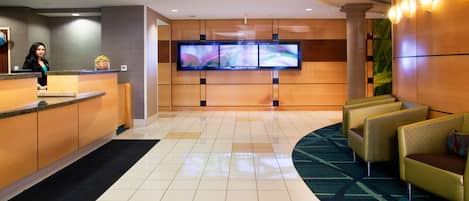 Zona de recepción de hotel con mostrador, televisor de pantalla plana en la pared y un área de descanso con sillones.
