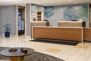 A reception area with a wooden reception desk, a Pepsi refrigerator, a potted plant, and a patterned rug. - SpringHill Suites by Marriott Medford (Medford)