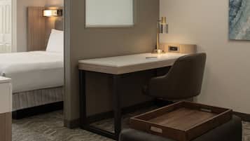 Quarto de hotel com cama, escrivaninha, cadeira, mesa de apoio e luminária na parede.