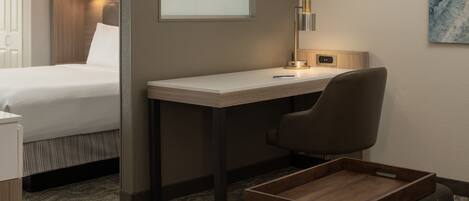 Une chambre d’hôtel équipée d’un lit, d’un bureau, d’une chaise, d’une petite table et d’une lampe fixée au mur.