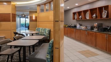 A modern hotel lobby with seating areas, a kitchen with wooden cabinets, and a view of the outdoors.