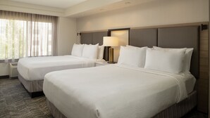 Habitación de hotel con dos camas, una mesita de noche con lámpara y un ventanal con cortinas.