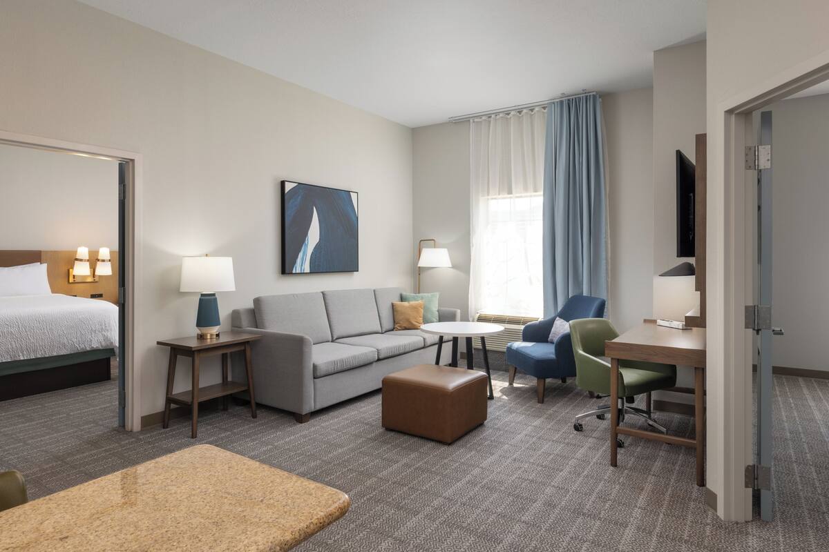 Una habitación de hotel con una cama, un sofá, un escritorio, una silla, una mesita y un televisor.