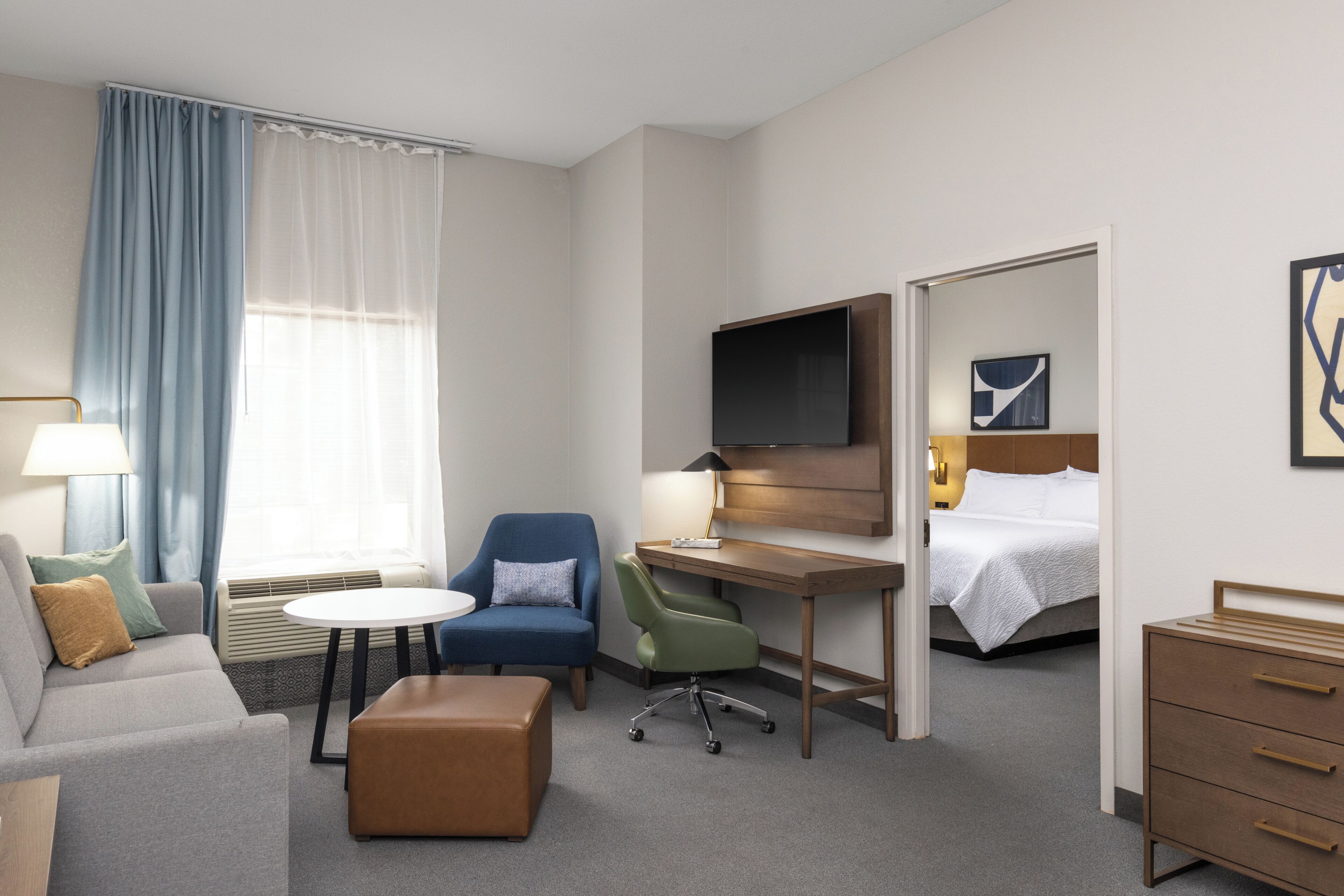 A hotel room with a sofa, a desk, a chair, a TV, a bed, and a dresser.