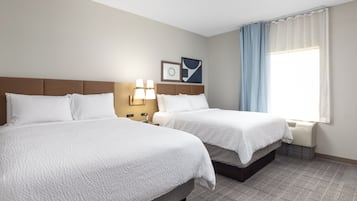 Une chambre d’hôtel avec deux lits, une fenêtre avec des rideaux, une lampe fixée au mur et un tableau encadré.