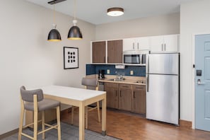 Eine moderne Küche mit einem weißen Tisch, zwei Barhocker, einer Mikrowelle, einem Kühlschrank und Holzschränken.