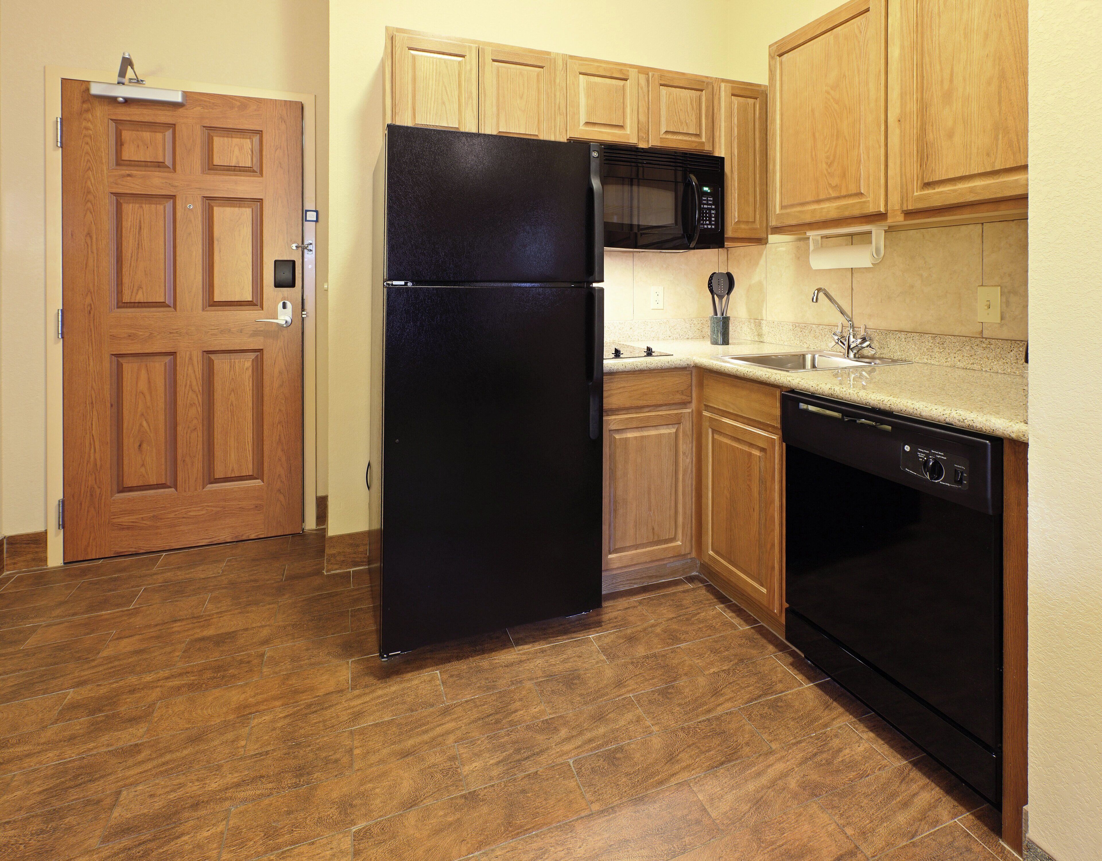 A kitchen with wooden cabinets, a black refrigerator, a microwave, and a dishwasher.