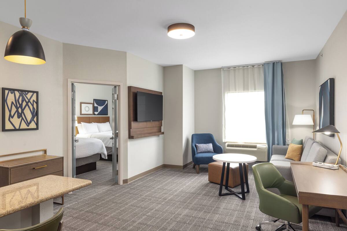 Habitación de hotel con cama, escritorio, silla, televisor y ventana con cortinas.