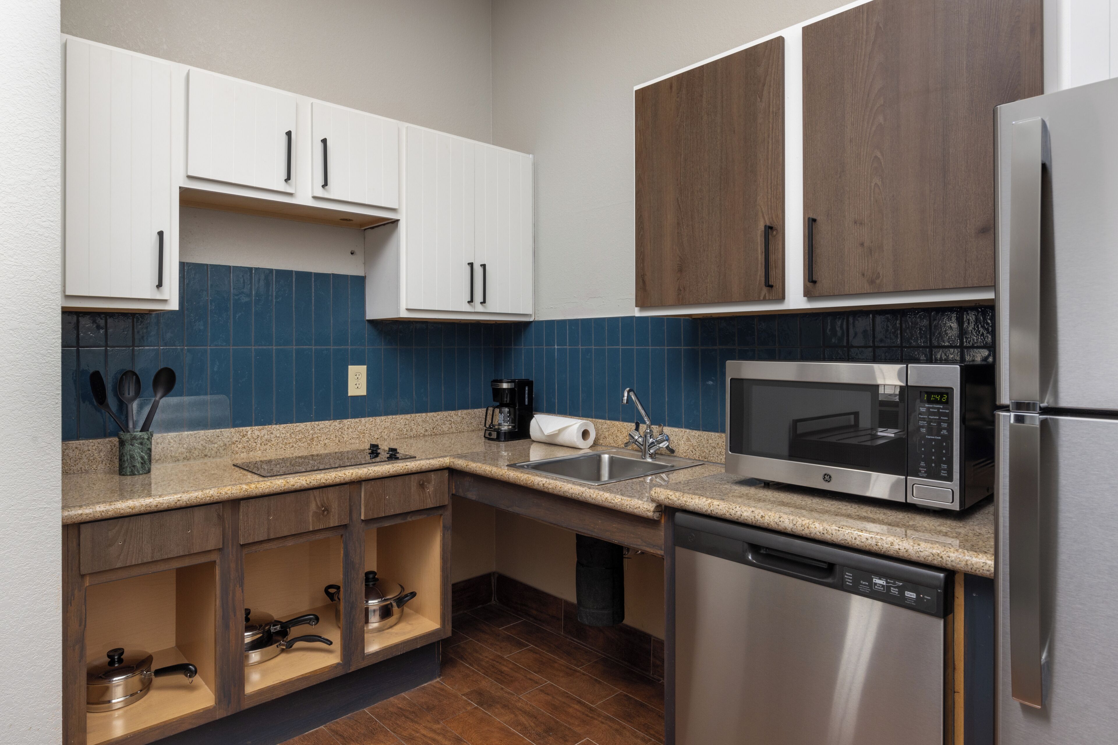 A modern kitchen with white and brown cabinets, a stainless steel refrigerator, a microwave, and a dishwasher.