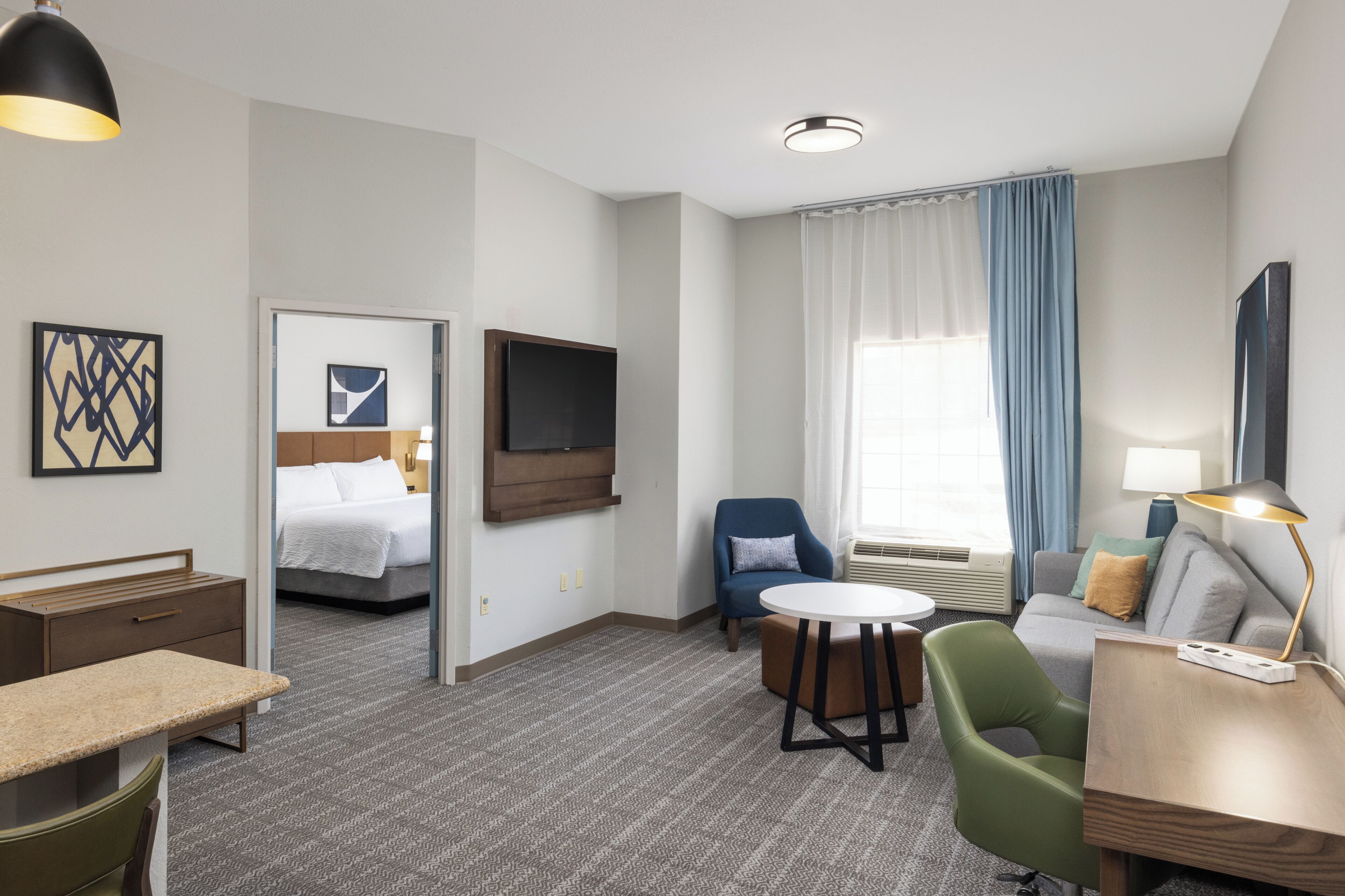 A hotel room with a bed, a desk, a chair, a sofa, a TV, and a window with curtains.