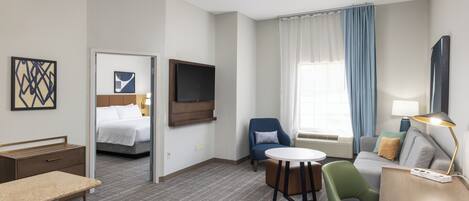 A hotel room with a bed, a desk, a chair, a sofa, a TV, and a window with curtains.
