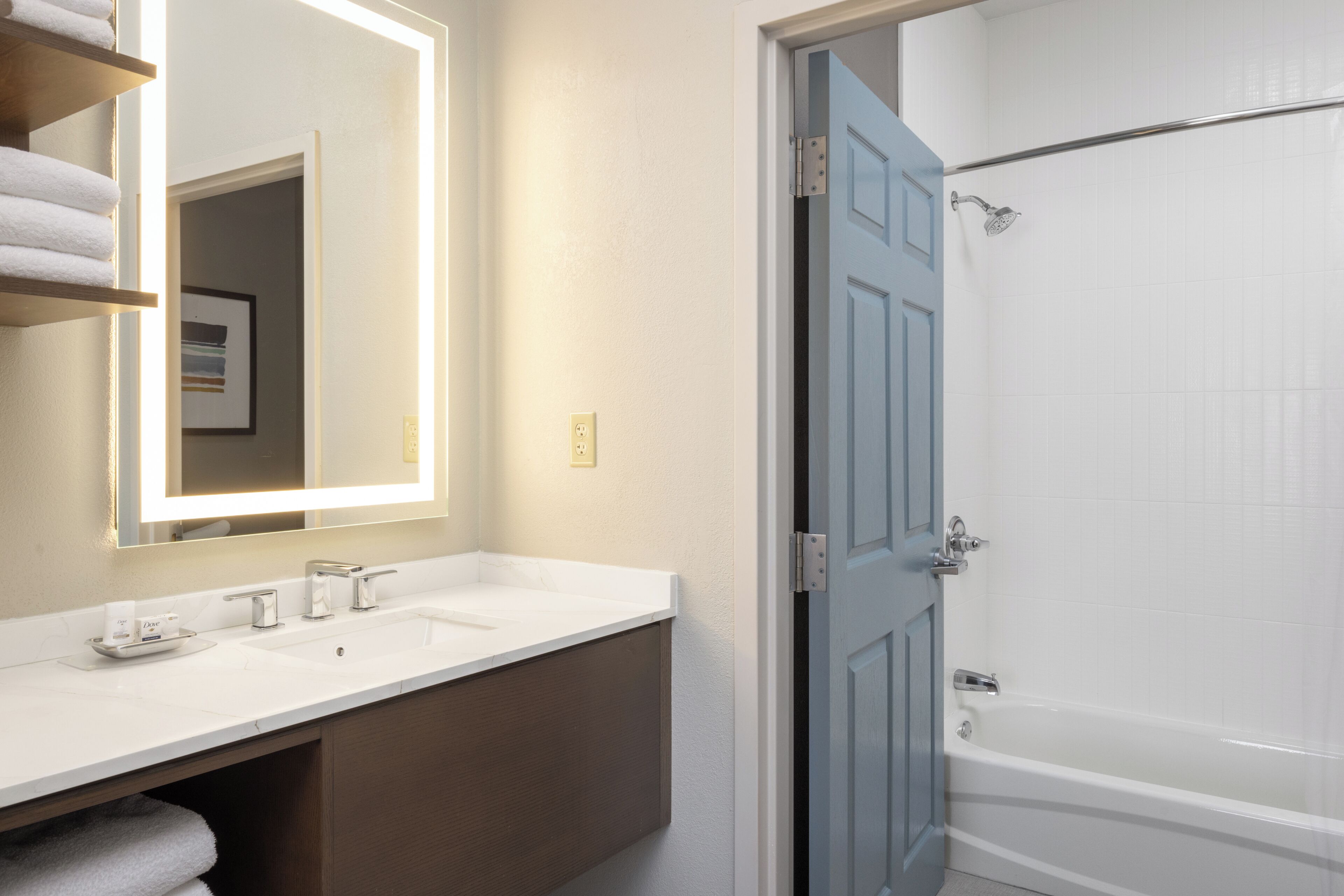 A bathroom with a white sink, a mirror, a towel rack, and a door leading to a shower area.