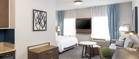 Habitación de hotel con cama, escritorio, silla, televisor y ventana con cortinas.