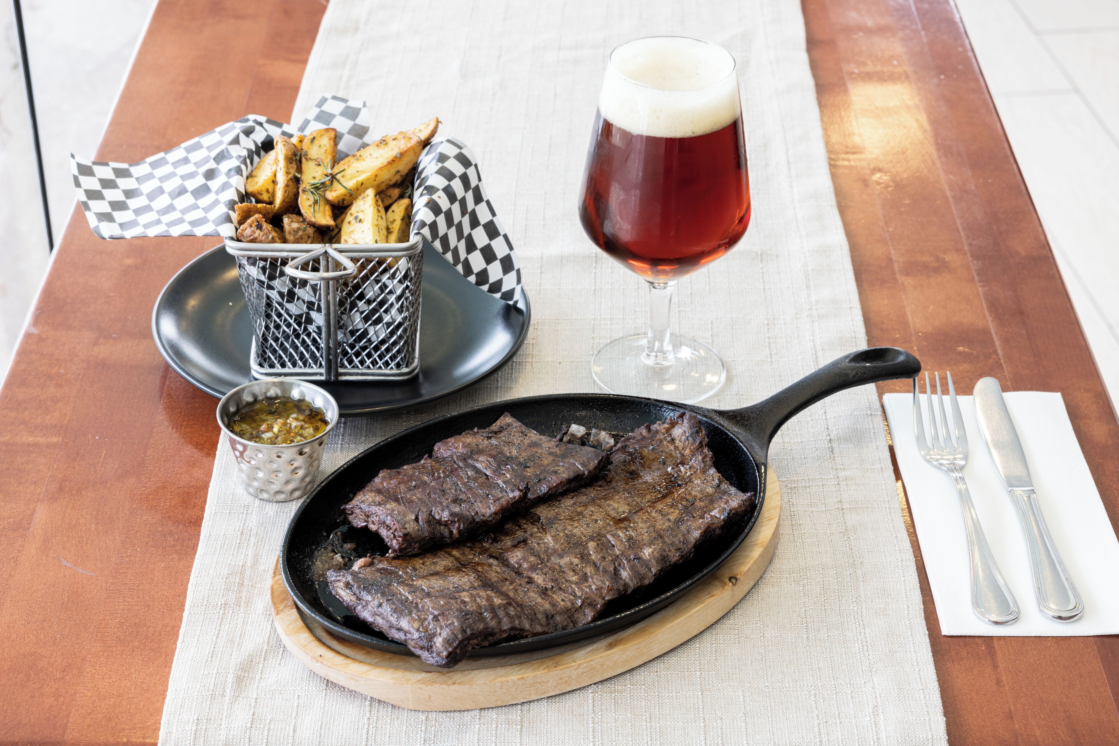 Un bistec, papas fritas y una cerveza sobre una mesa de madera.