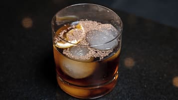 Un verre de thé glacé, une tranche de citron et une pincée de poudre brune sur une surface sombre.