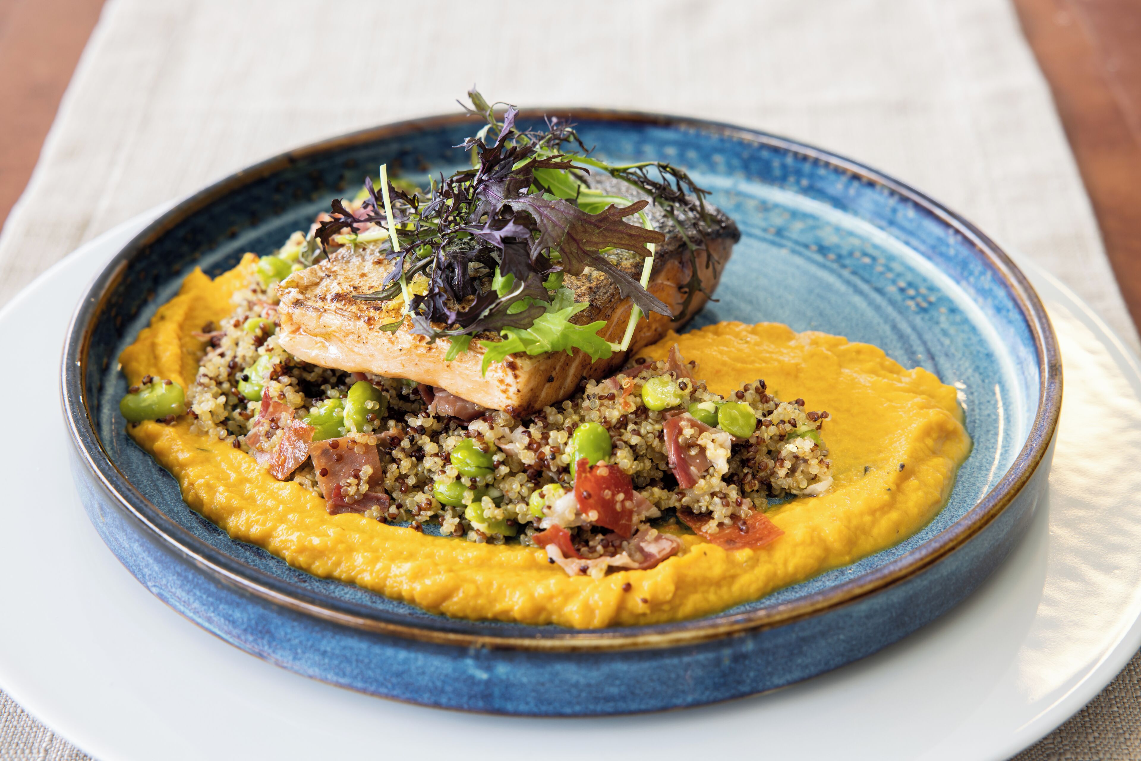 Une assiette de nourriture contenant du quinoa, des légumes verts et un morceau de viande, le tout servi dans une assiette bleue.
