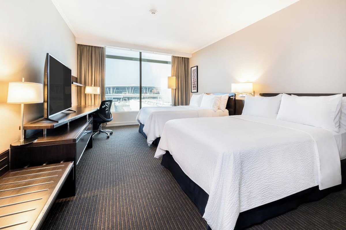 A hotel room with two beds, a TV, a desk, and a view of a bridge.