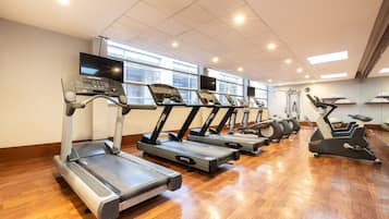 Un gimnasio con varias cintas de correr alineadas frente a una pared con ventanas.