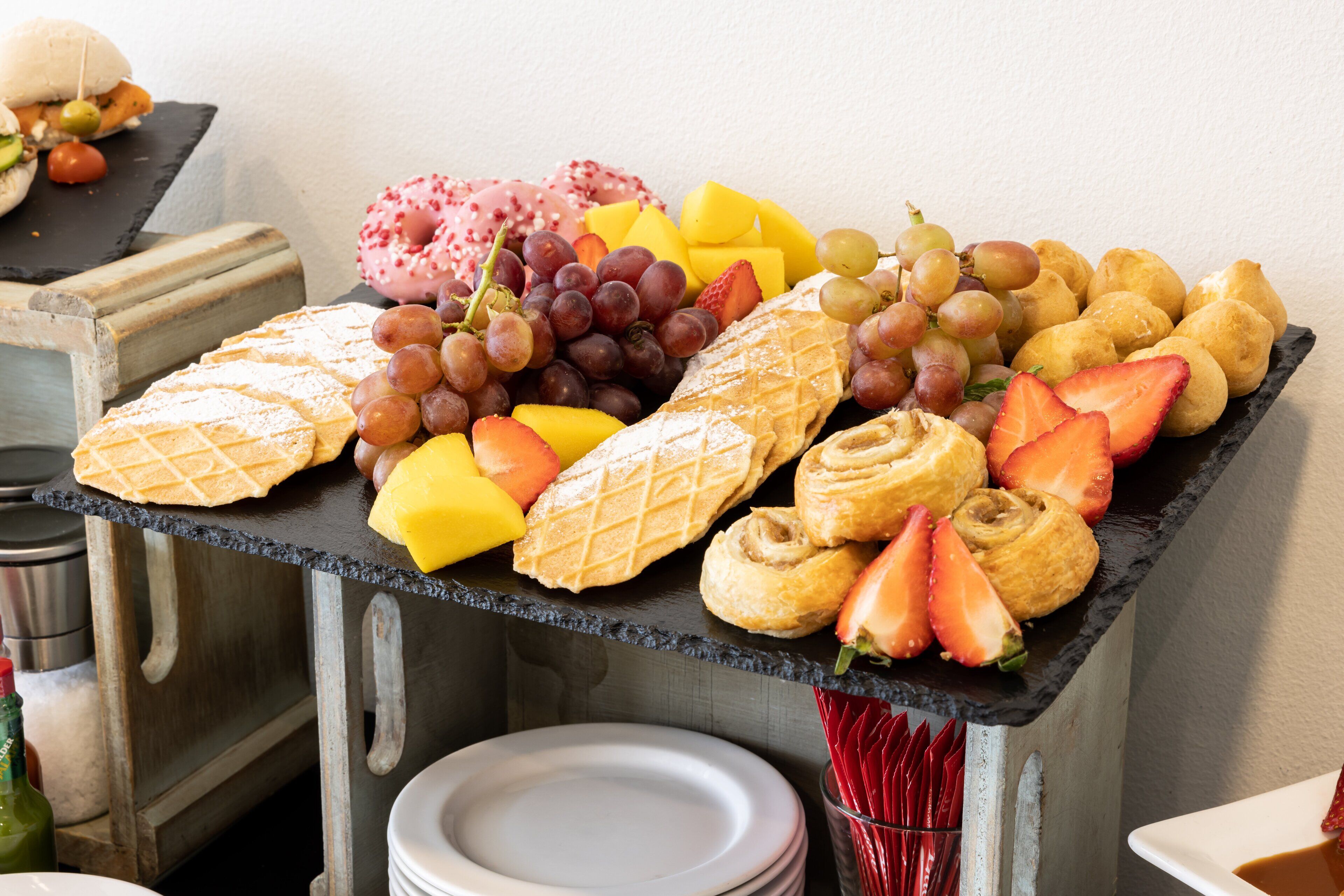A buffet table with a variety of pastries, fruits, and a waffle.