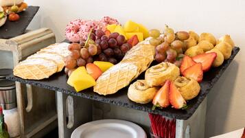 Una mesa de buffet con una variedad de pasteles, frutas y un waffle.