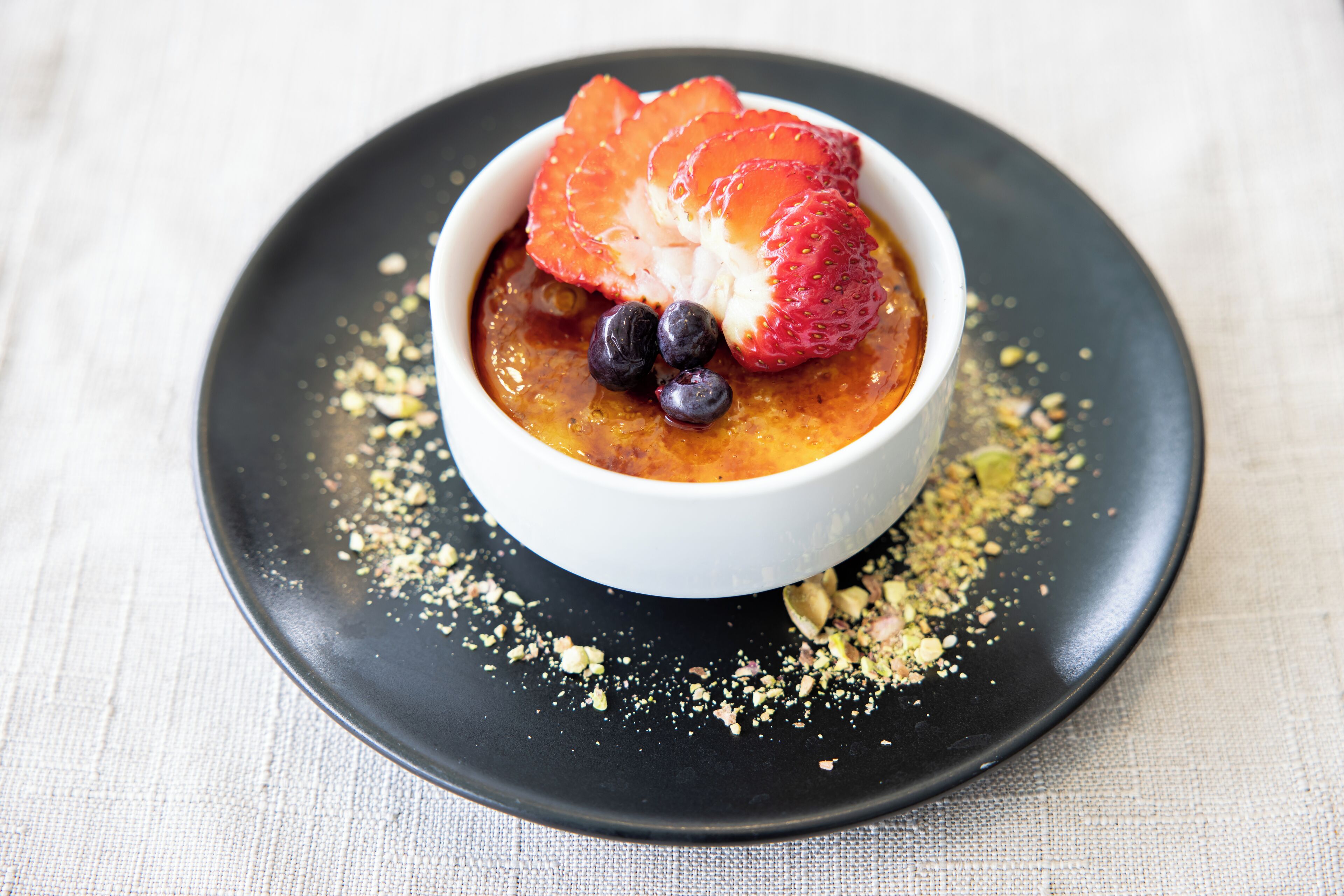 Un postre en un tazón blanco sobre un plato negro, decorado con fresas y arándanos.