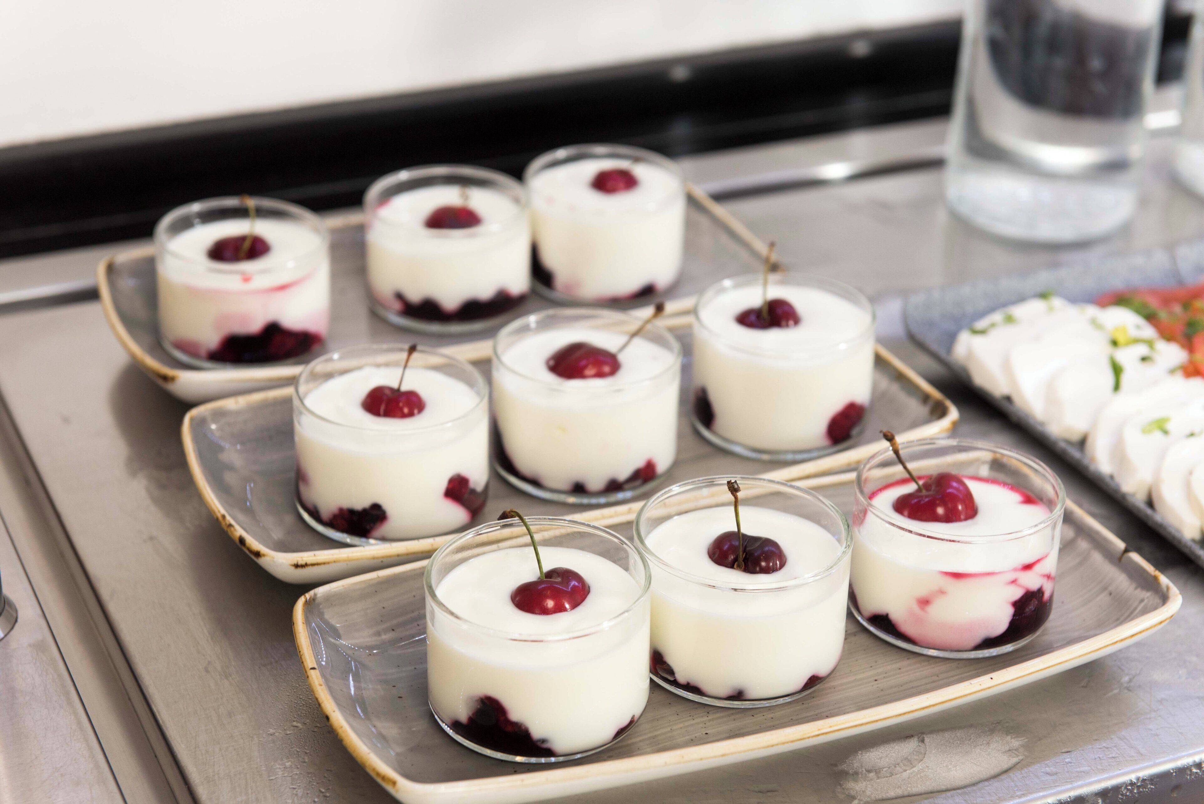 Una bandeja con copas de postre y cerezas sobre una superficie metálica.