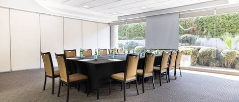 Un salón de conferencias con una larga mesa, sillas y una pantalla para proyector.
