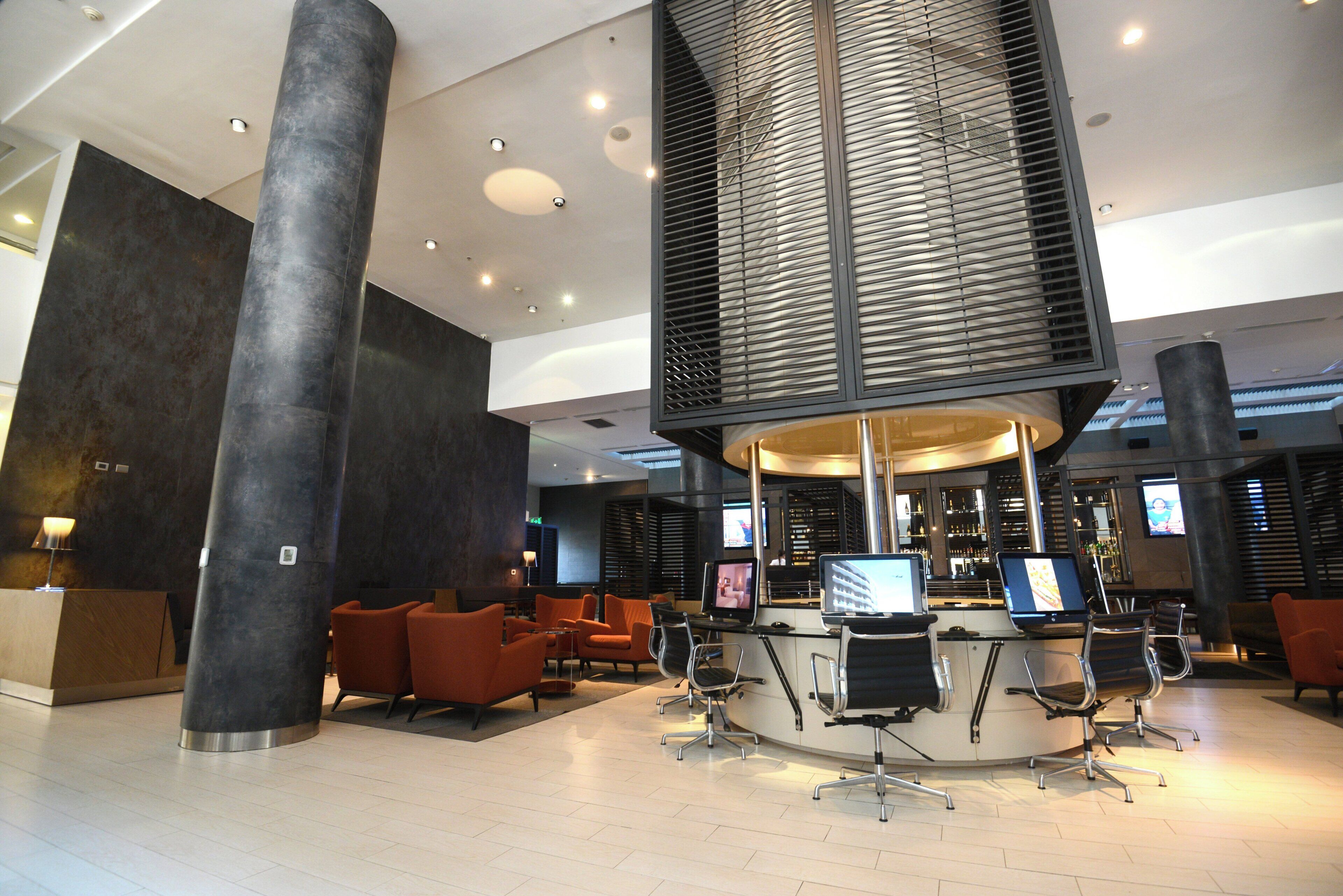 A modern lobby with a central column, seating area, and multiple screens.