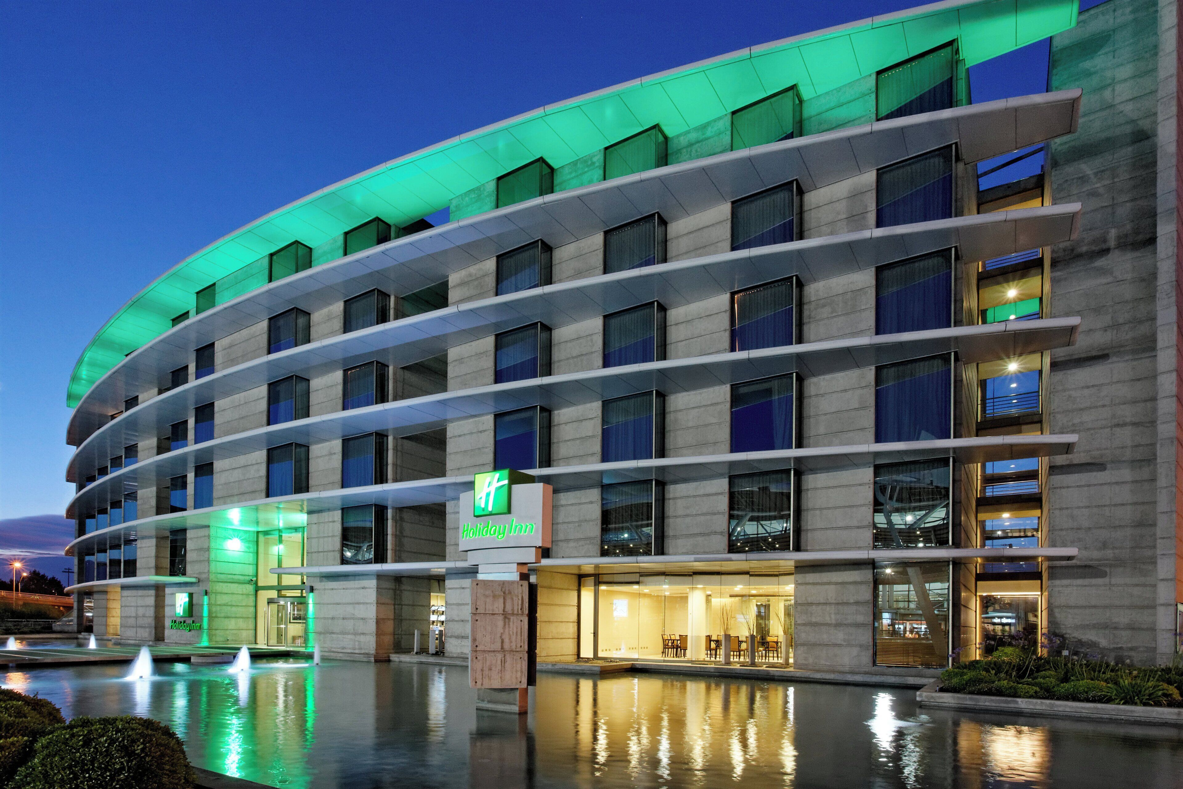 A Holiday Inn hotel with a curved facade, multiple floors, and a reflective pool in the foreground.