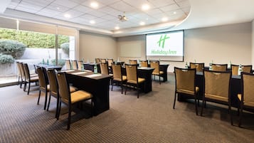 A conference room with a projector screen displaying "Holiday Inn" and a large window overlooking a garden.