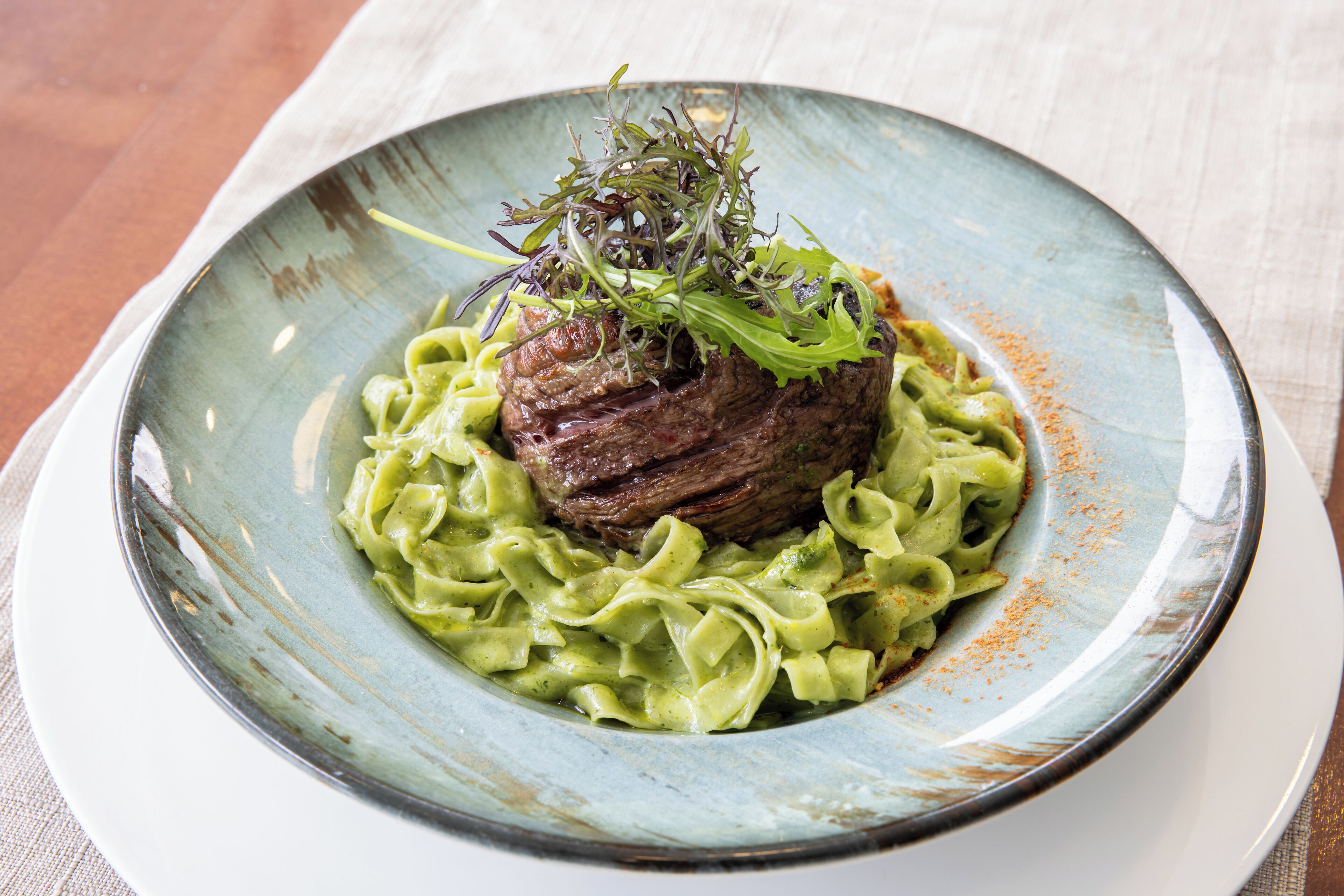 Un plato de pasta con un centro de carne, cubierto con vegetales verdes, servido en un plato de cerámica.