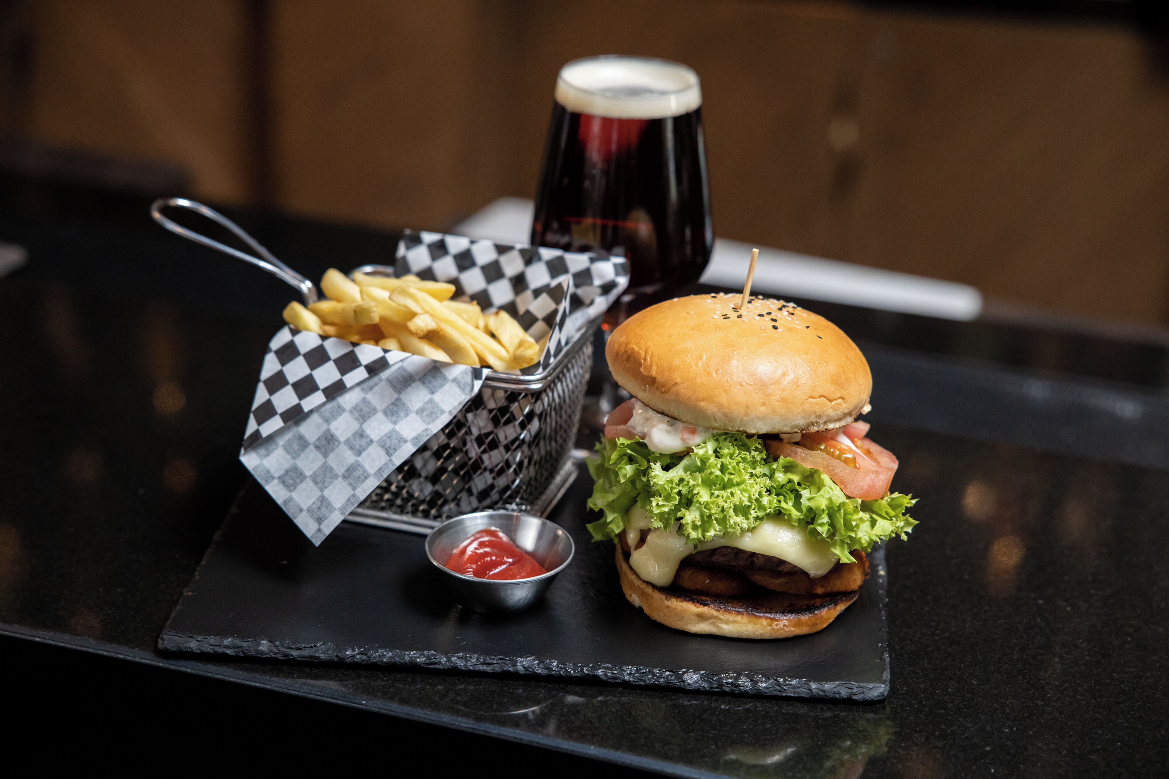 A burger with fries and a drink on a black slate serving tray.