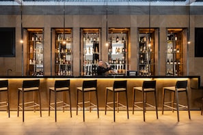 Un espace bar avec de nombreuses étagères remplies de bouteilles, un barman et plusieurs tabourets de bar.