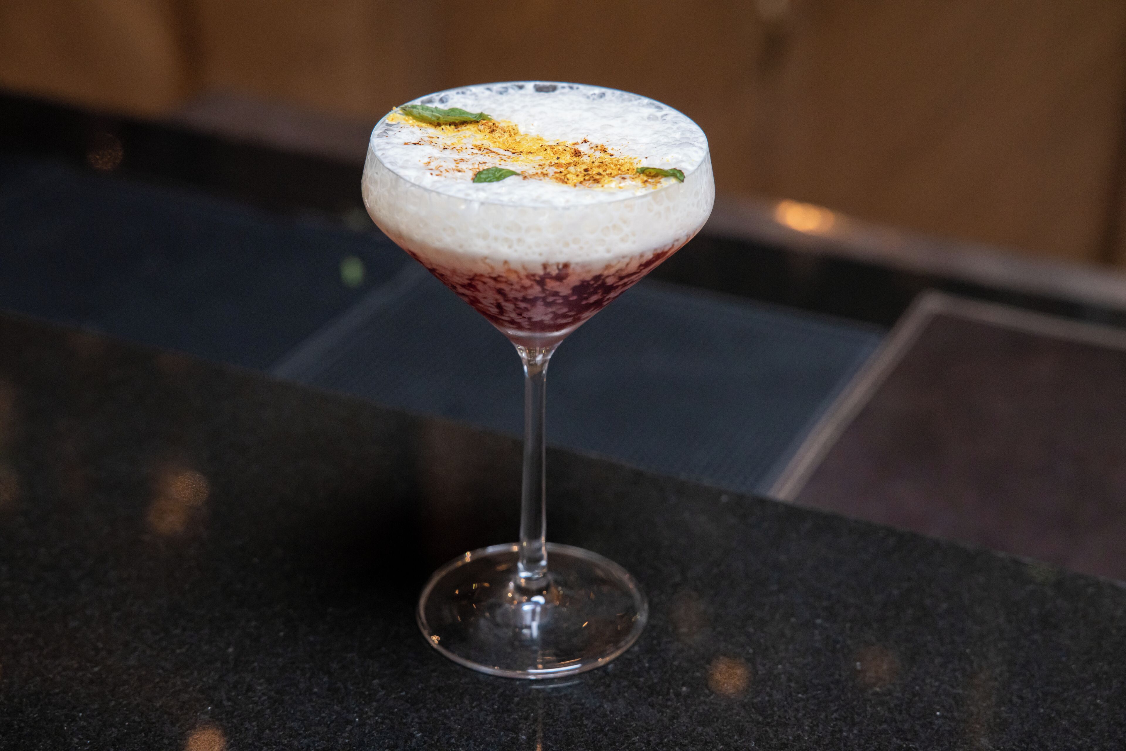 Un cóctel en una copa de martini sobre una encimera oscura.