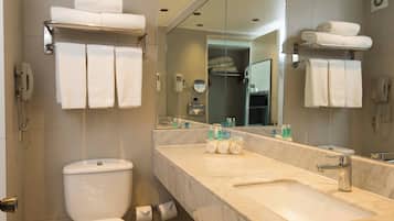 Een badkamer met toilet, wastafel en spiegel. Handdoeken liggen op een rek en er hangt een telefoon aan de muur.