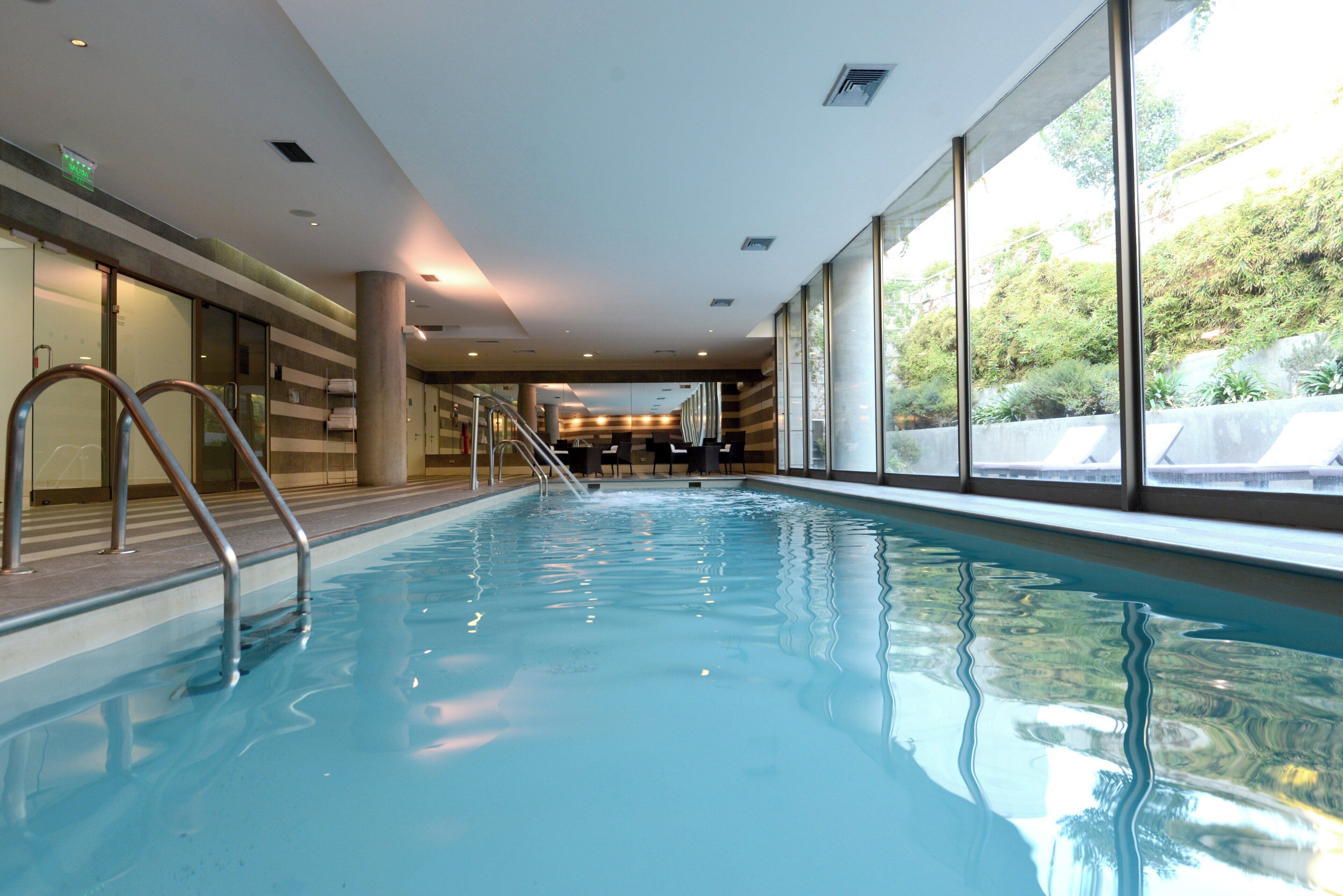 Una piscina interior con agua cristalina, una escalera metálica y vistas al exterior a través de amplias ventanas.