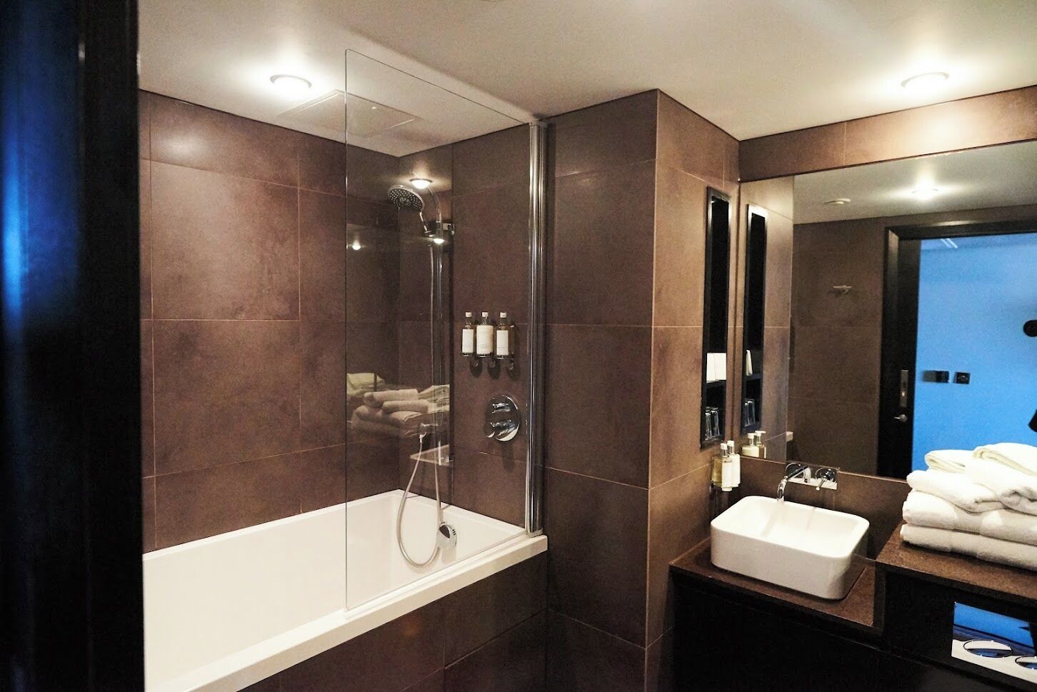 Un baño moderno con ducha de vidrio, una bañera blanca y un lavamanos con lavabo y espejo.