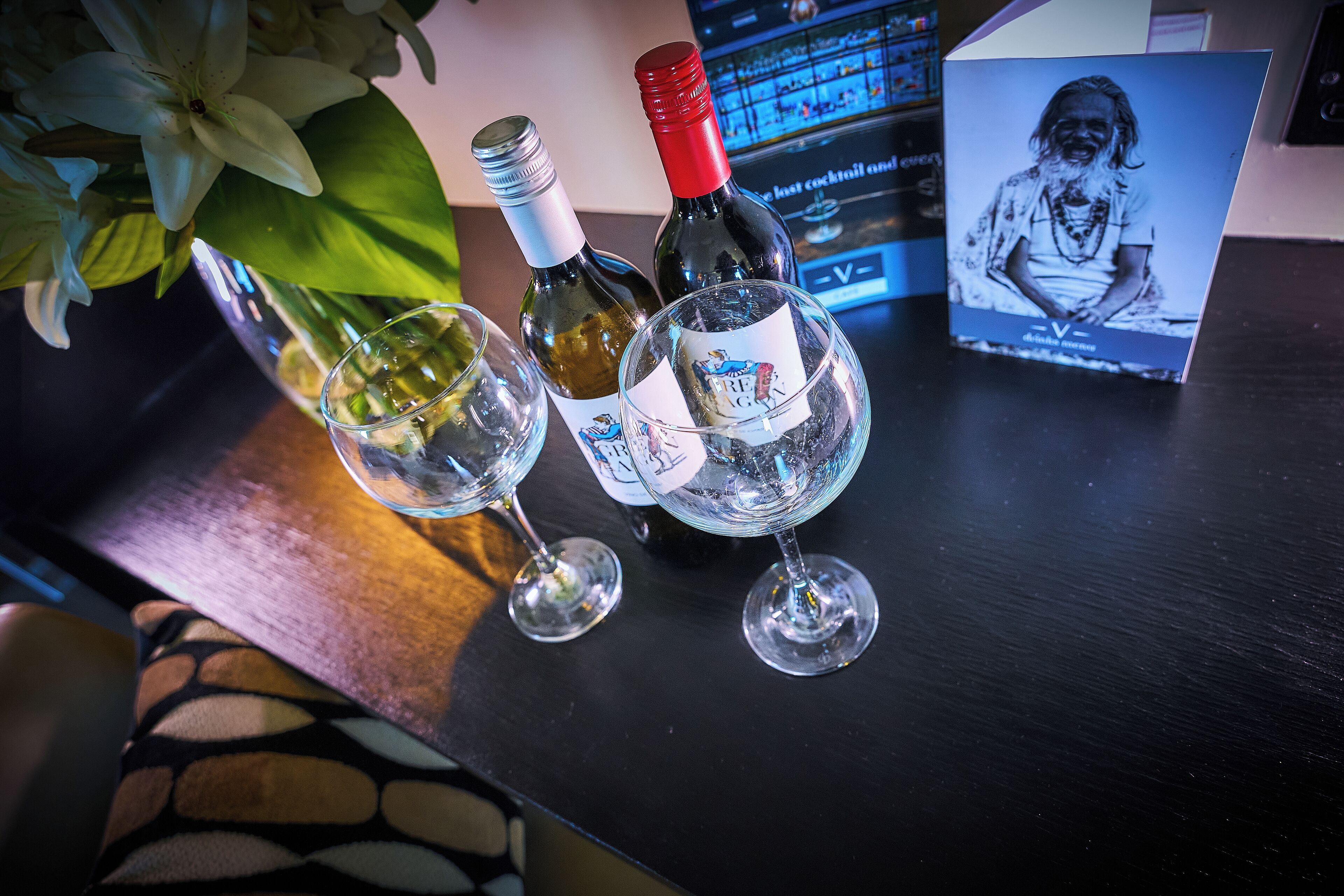 A bar area with two wine glasses, a bottle of wine, and a menu board.