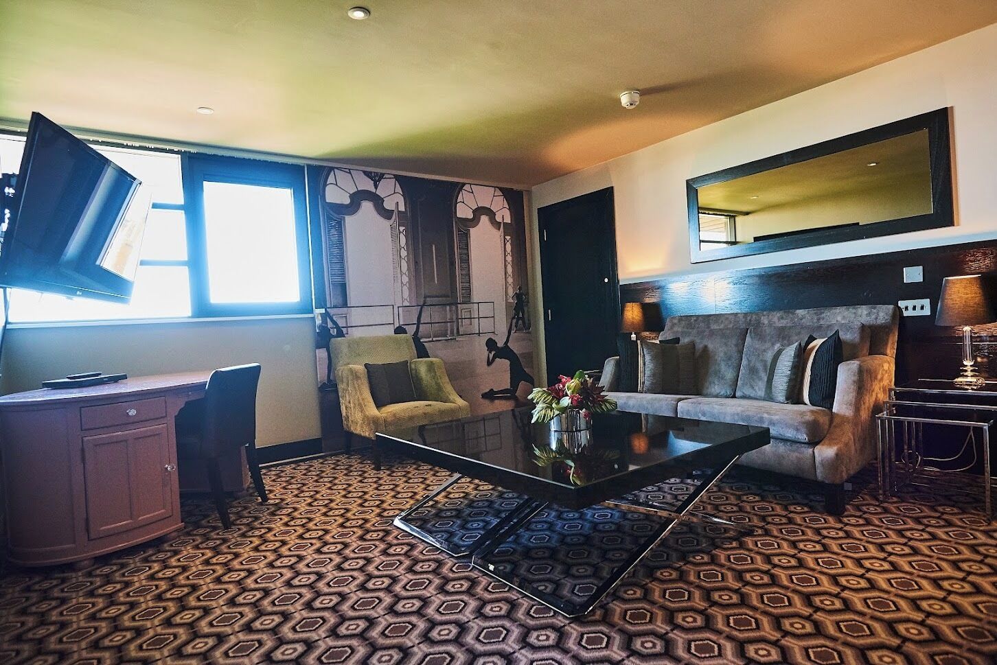 A room with a desk, two armchairs, a sofa, a coffee table, and a patterned carpet.