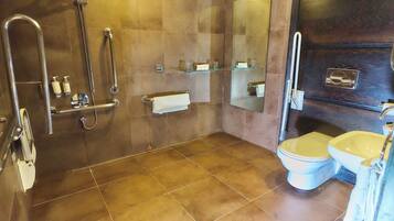 A bathroom with a shower, toilet, and sink, equipped with grab bars and a towel rack.