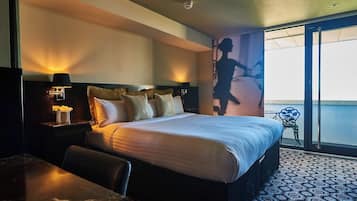 Ein Hotelzimmer mit Bett, Nachttisch mit Lampe, Stuhl, Tisch und einem Balkon mit Blick.