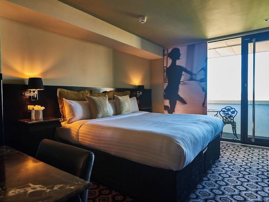 Ein Hotelzimmer mit Bett, Nachttisch mit Lampe, Stuhl, Tisch und einem Balkon mit Blick.