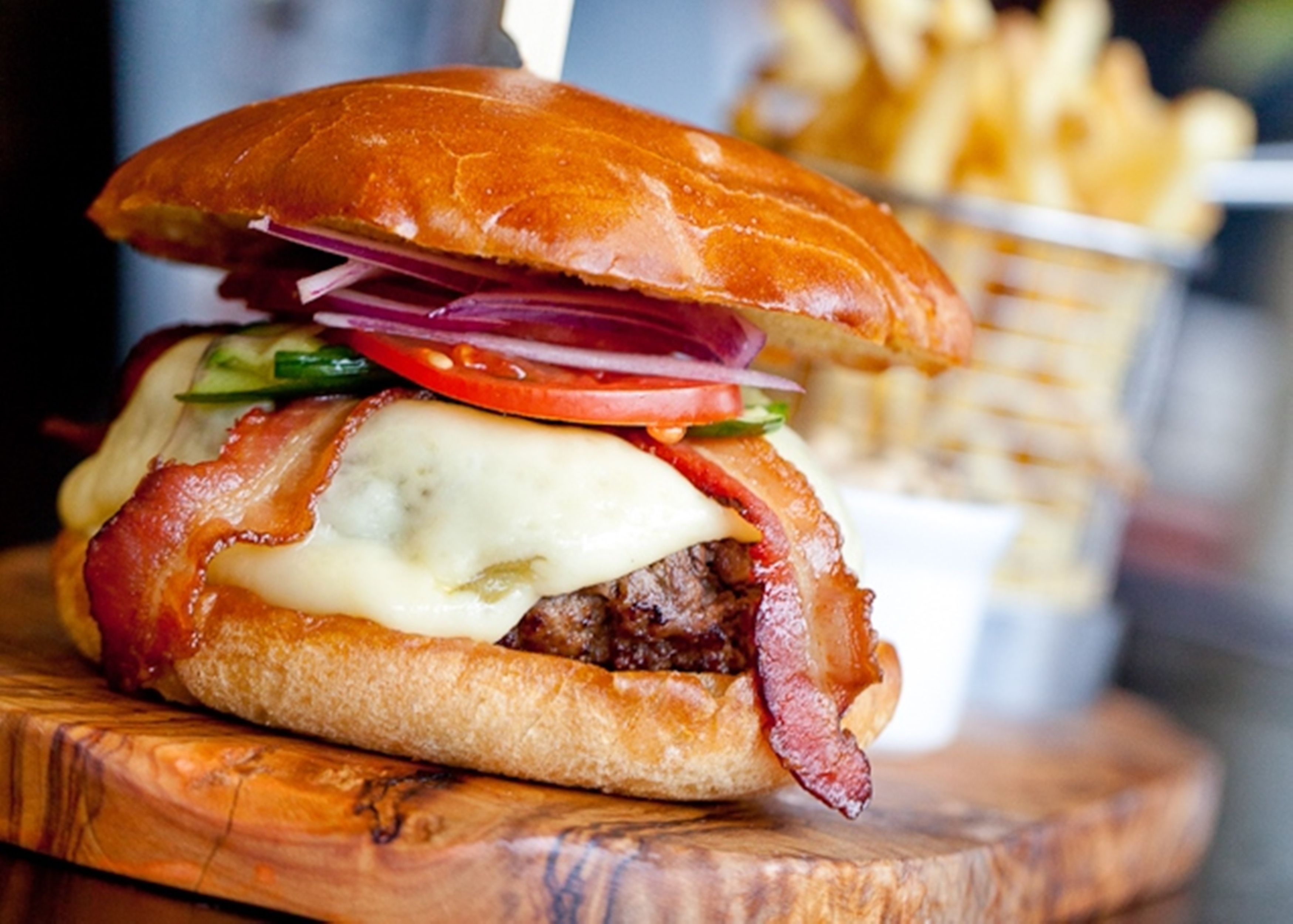 Hamburguesa con tocino, queso y vegetales, acompañada de papas fritas.